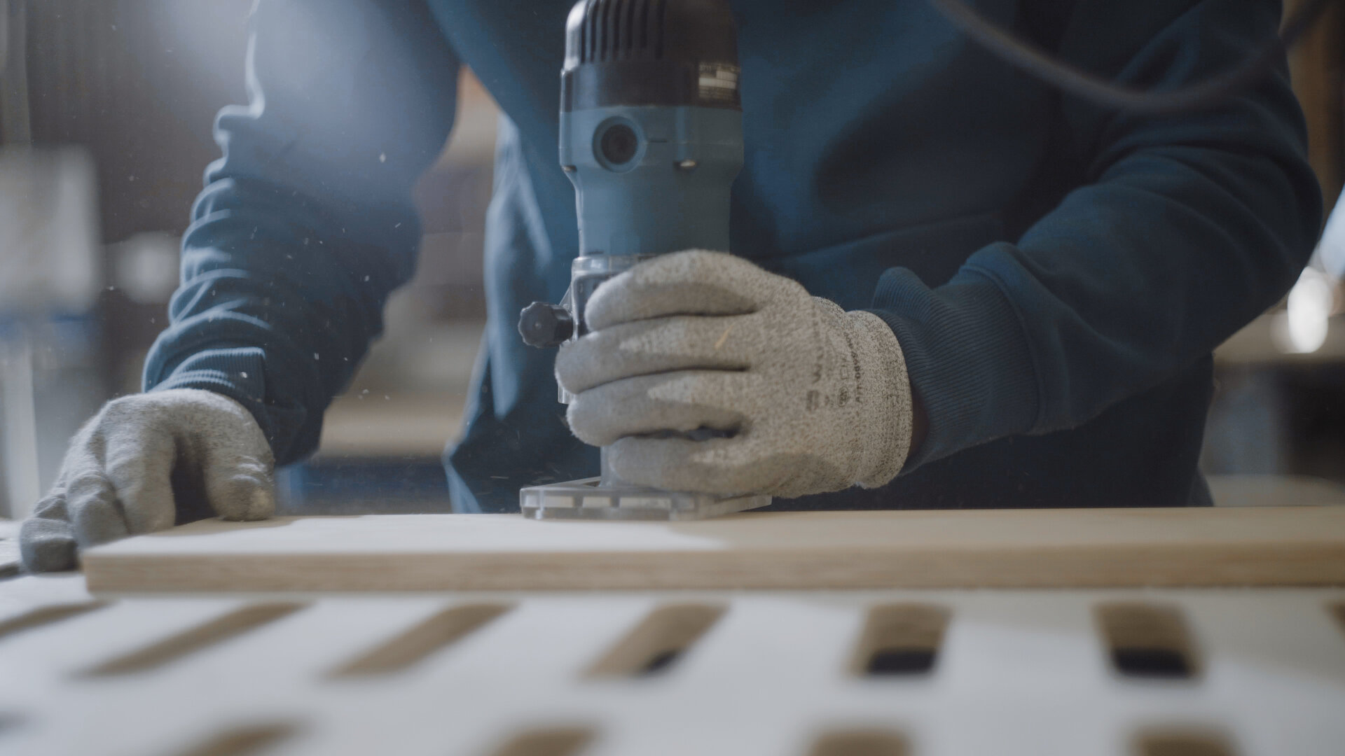 Eine Person mit Schutzhandschuhen bearbeitet eine Holzplatte